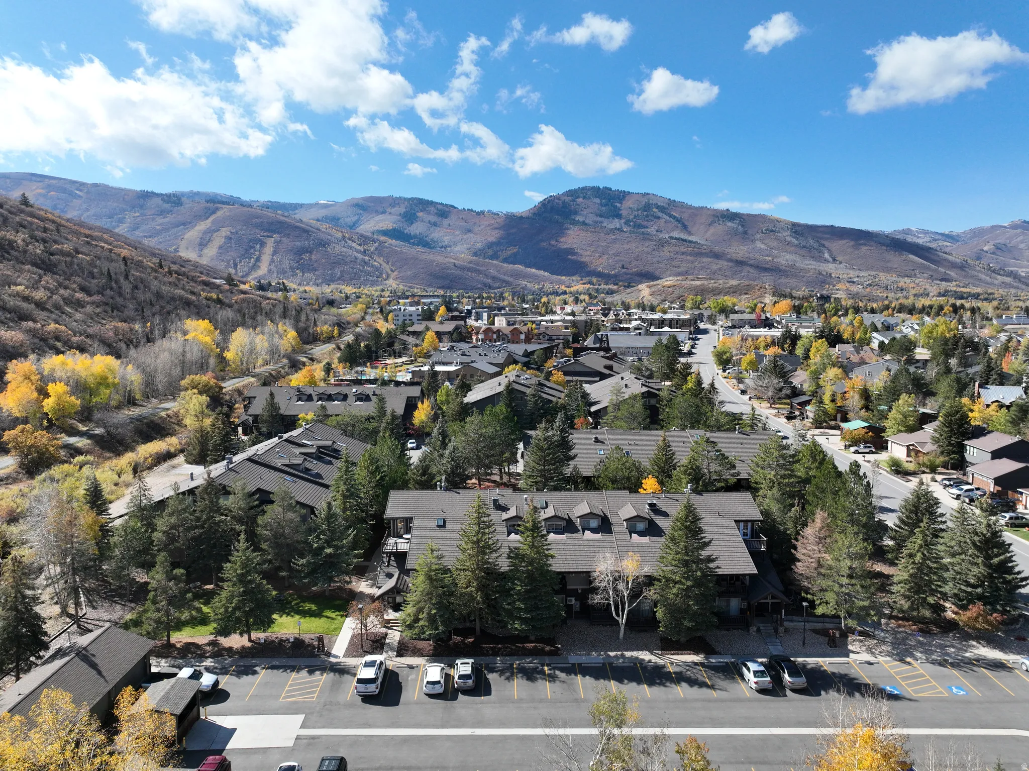 Expansive mountain landscape featuring a vibrant residential area, multiple multi-story buildings, abundant evergreen trees, and a visible parking area
