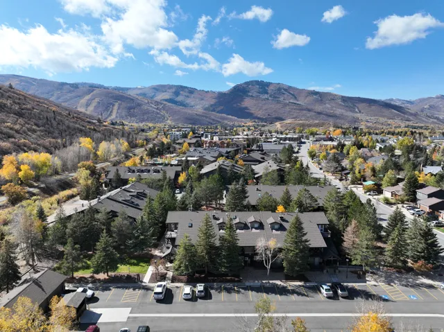 Expansive mountain landscape featuring a vibrant residential area, multiple multi-story buildings, abundant evergreen trees, and a visible parking area