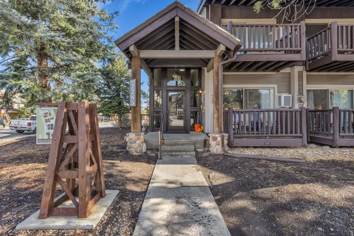 Building entrance featuring a covered porch with exposed beams, stone column bases, and a glass paneled door