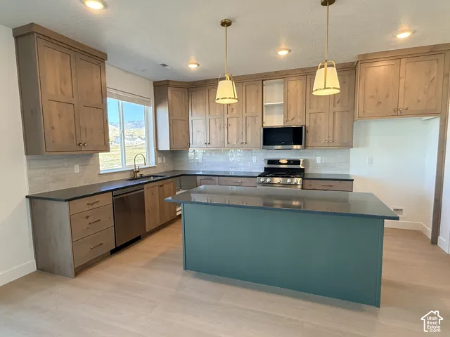 Kitchen featuring a central island, wood-finish cabinetry, dark countertops, stainless steel appliances, and a tiled backsplash