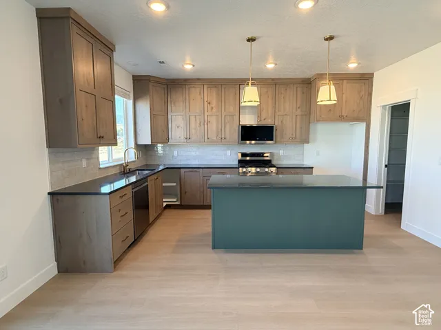 Kitchen with wood-finish cabinetry, dark countertops, a contrasting island, stainless steel appliances, and pendant lighting