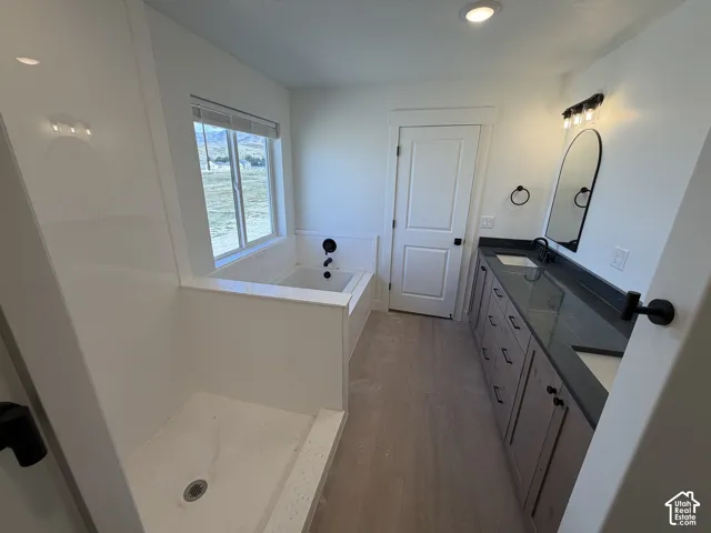 Contemporary bathroom featuring a built-in tub, separate shower, double vanity with dark countertops, and wood-finish flooring