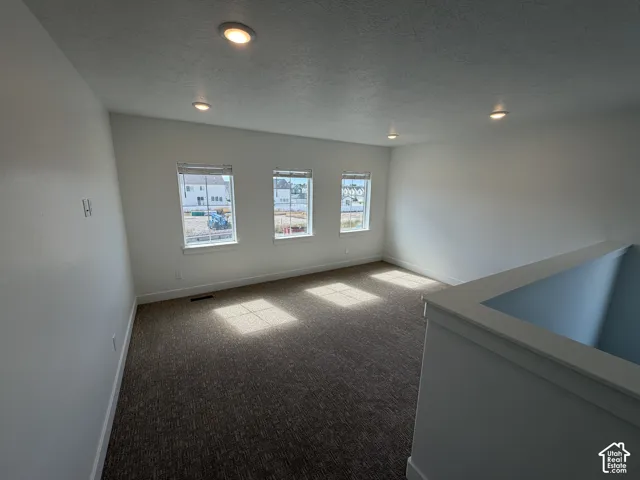 Recessed lighting, three windows with blinds, light-toned walls, and textured carpet flooring
