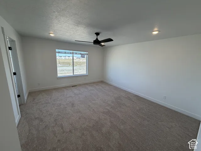 Spacious room featuring neutral carpeting, a large window, a ceiling fan, and recessed lighting