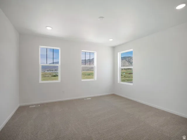 Bright room featuring three windows, recessed lighting, and neutral carpeting
