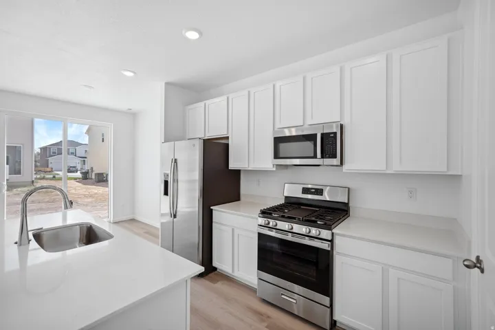 Modern kitchen featuring white shaker cabinetry, stainless steel appliances, light-toned countertops, a stainless steel sink with a gooseneck faucet, and light wood-finish flooring