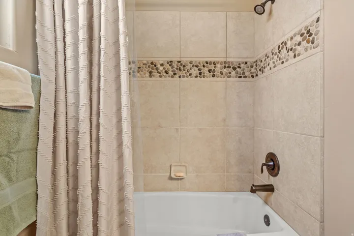 Tub and shower combination featuring tiled walls with a pebble accent band, bronze-finish fixtures, and a mounted showerhead