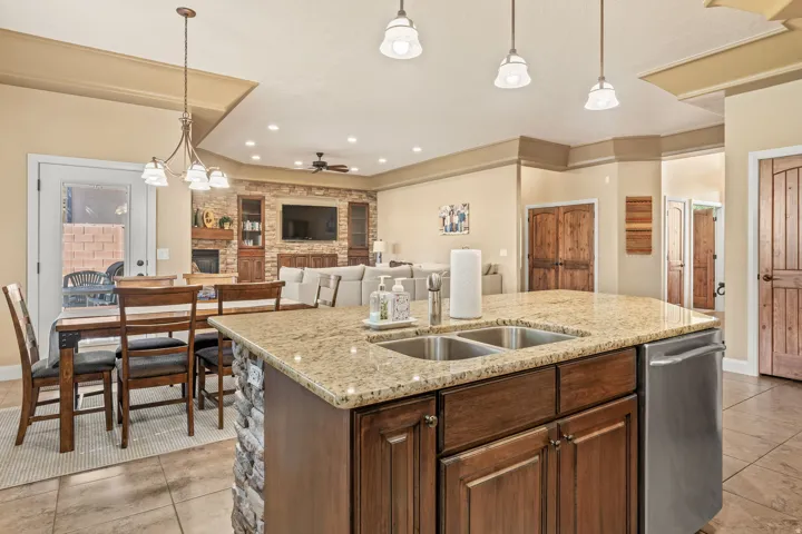 Kitchen island featuring a double-basin stainless steel sink, granite countertop, and dark wood cabinetry with stone veneer