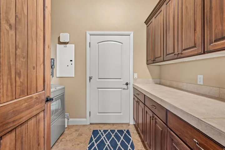 Utility room with wood-finish cabinetry, light-toned countertop, and tile flooring