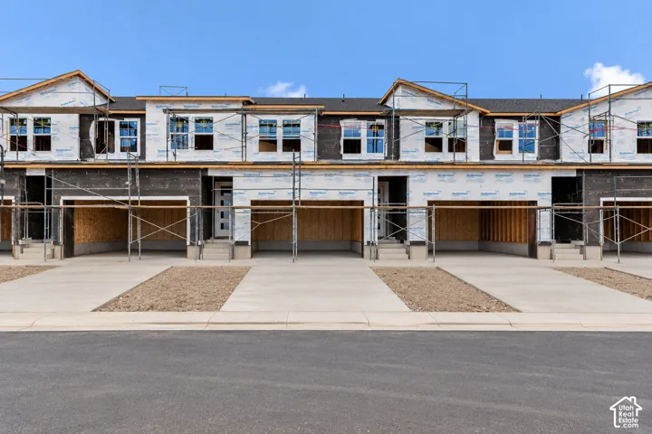 Multi-story townhomes under construction featuring individual garage bays, concrete driveways, and multiple window openings