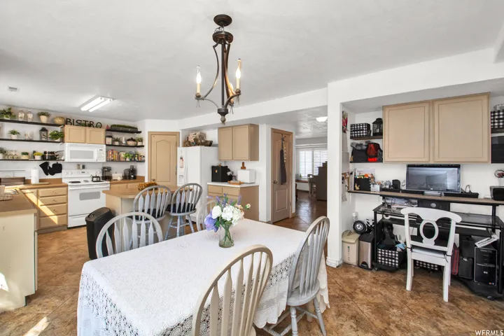 Kitchen and dining area featuring a central chandelier, wood-finish flooring, light-toned cabinetry, white appliances, and open shelving