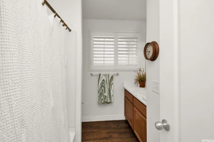 Bathroom featuring a wood-finish vanity with a white countertop, under-mount sink, and a window with plantation shutters