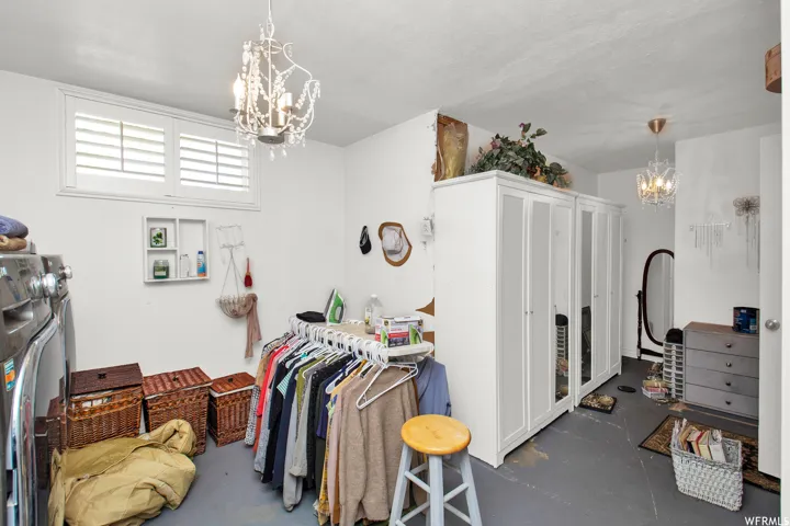 Room featuring two decorative chandeliers, a window with white louvered shutters, and gray-painted flooring