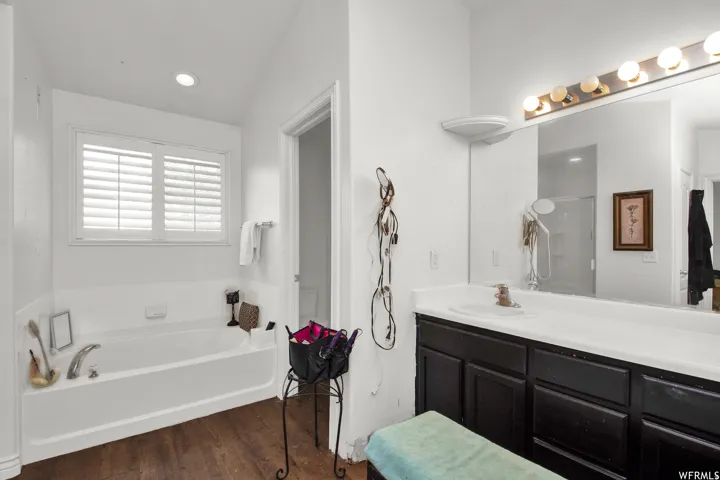 Bathroom featuring a built-in tub with chrome fixtures, wood-finish flooring, and white plantation shutters