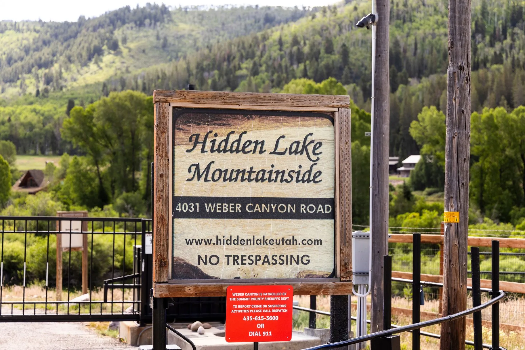 Entry sign to Hidden Lake Mountainside, featuring a natural wood frame, black metal fencing, and a mountainous, treed backdrop