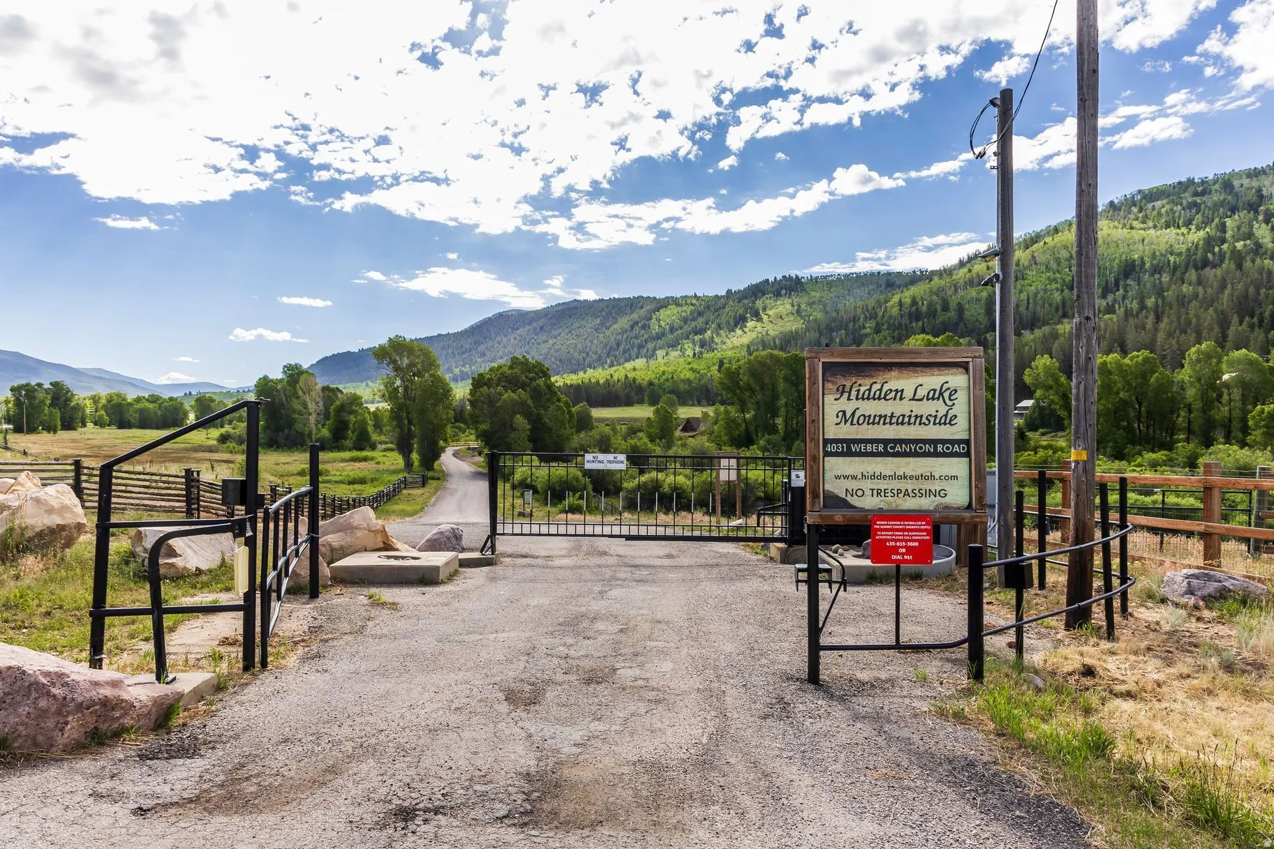 Gated entry to a private community with a paved road, natural rock landscaping, and surrounding mountainous terrain