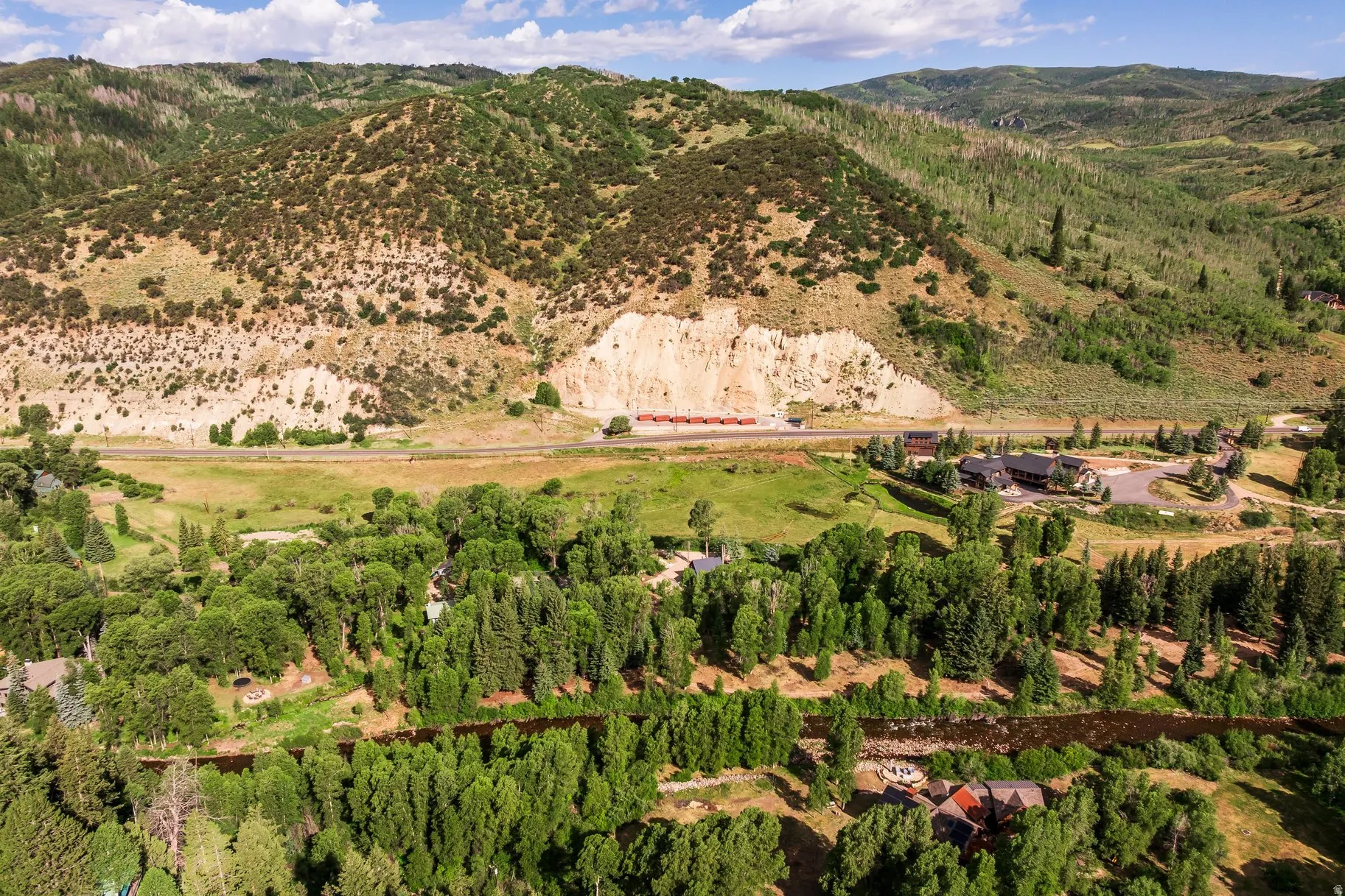 Expansive property featuring a forested river, multiple residences, and a backdrop of verdant mountains