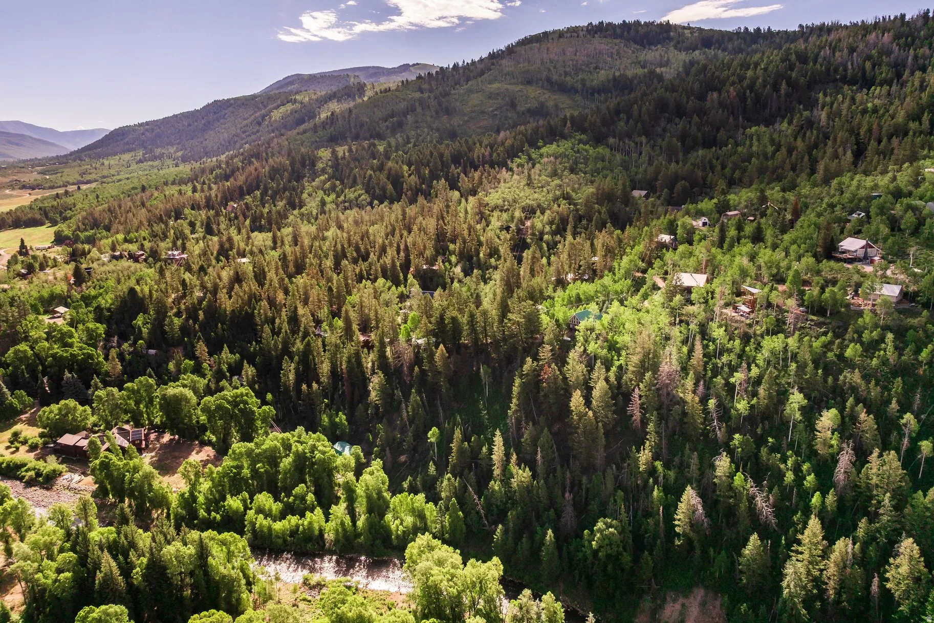 Expansive mountainous landscape featuring dense forestation, a river, and multiple residential structures