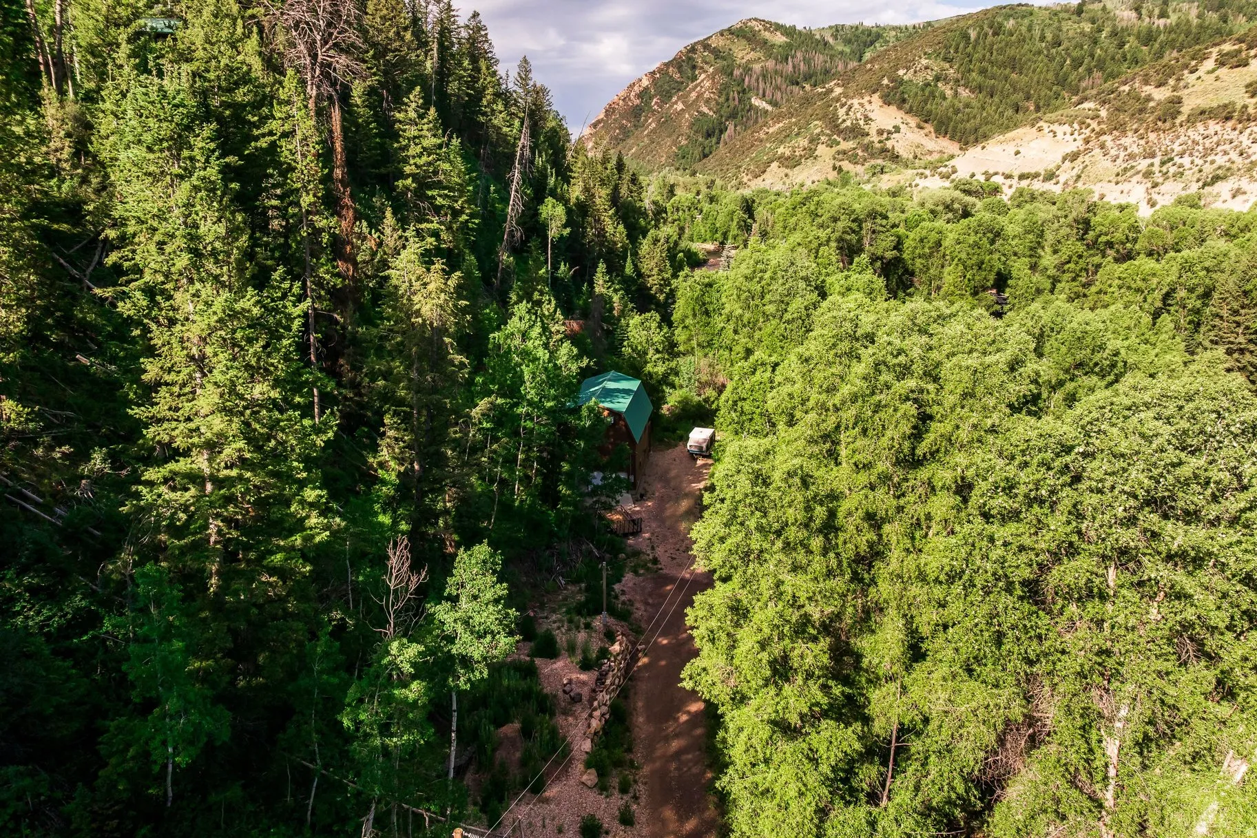 Mountainous landscape featuring a verdant valley, dense tree coverage, and an unpaved road