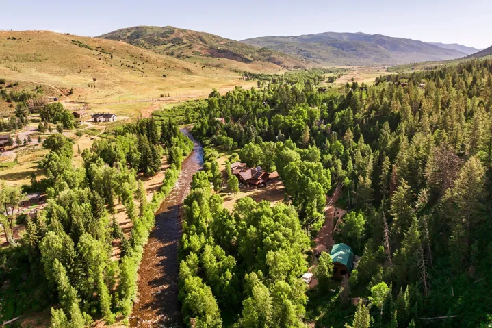 Expansive natural landscape featuring a winding river, dense forest, rolling hills, and multiple residential structures