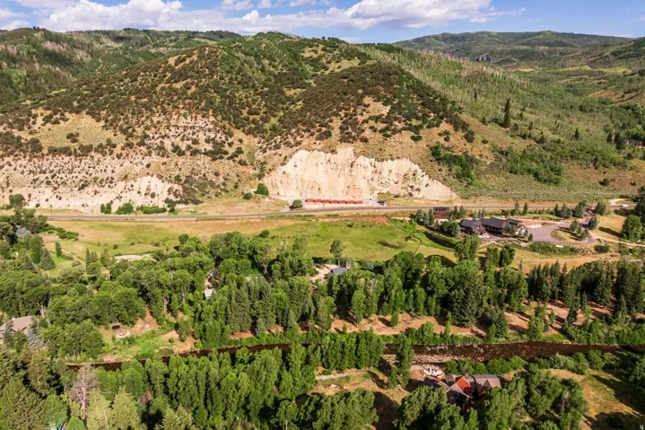 Expansive property featuring a forested river, multiple residences, and a backdrop of verdant mountains