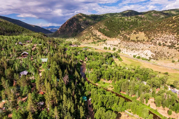 Expansive mountain valley setting featuring a river, dense forest, scattered residences, and a distant road