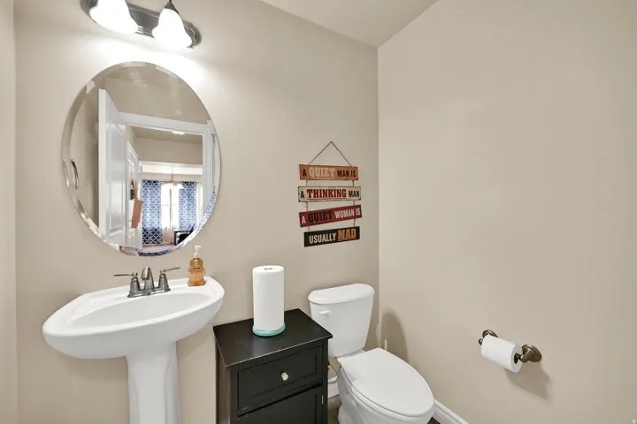 Pedestal sink with chrome-finish faucet, accompanied by an oval mirror with beveled edge