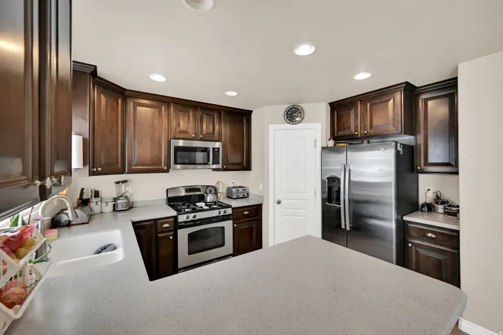 Kitchen featuring dark wood cabinetry, light-toned countertops, a stainless steel gas range, and a stainless steel refrigerator