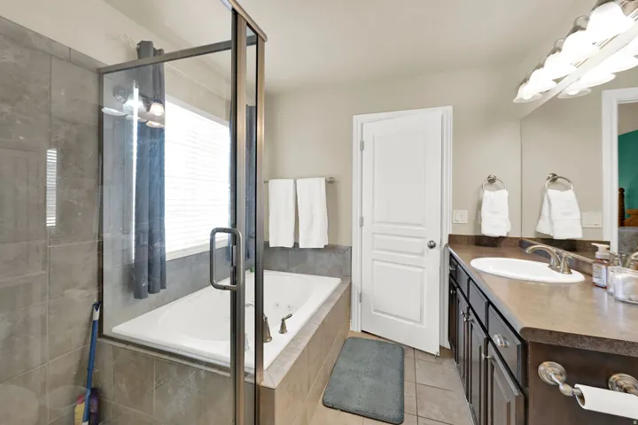 Spacious bathroom featuring a glass-enclosed shower, a separate soaking tub with tiled surround, a vanity with an integrated sink and dark cabinetry, and tile flooring