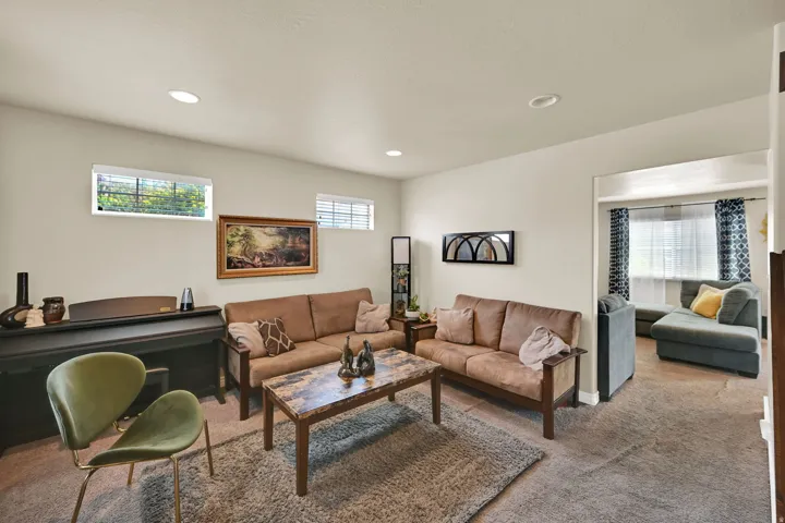 Carpeted living area featuring recessed lighting, light-toned walls, and a rectangular opening to an additional room with a window