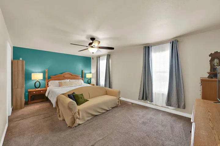 Spacious bedroom featuring warm neutral walls, an accent wall, two large windows with blinds, and a ceiling fan with integrated lighting