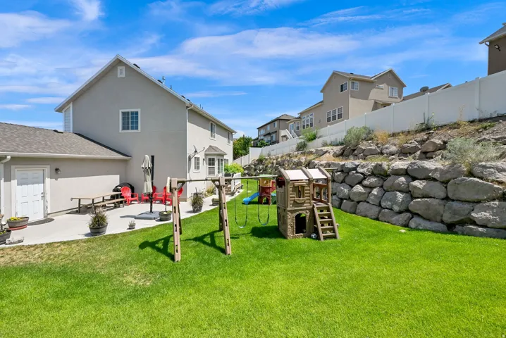 Expansive backyard featuring a lush lawn, a concrete patio, and a natural rock retaining wall