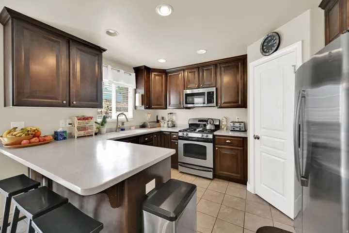 Kitchen featuring dark wood cabinetry, light-colored countertops, stainless steel appliances, recessed lighting, and tile flooring