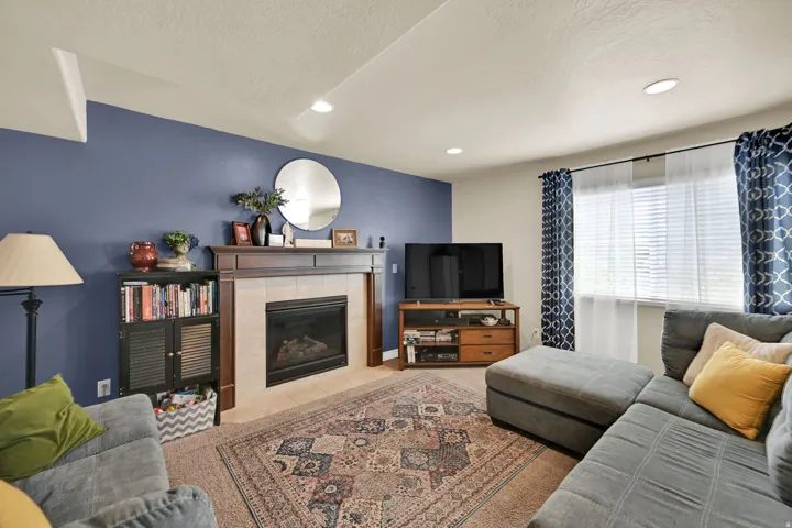 Living area featuring a fireplace with a wood-finish mantel and tile surround, recessed lighting, and a large window with blinds