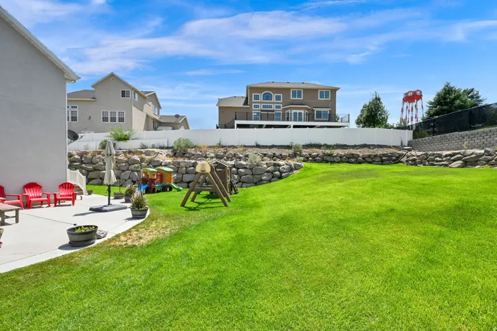 Spacious backyard featuring a large concrete patio, expansive lawn, and tiered landscaping with natural stone retaining walls