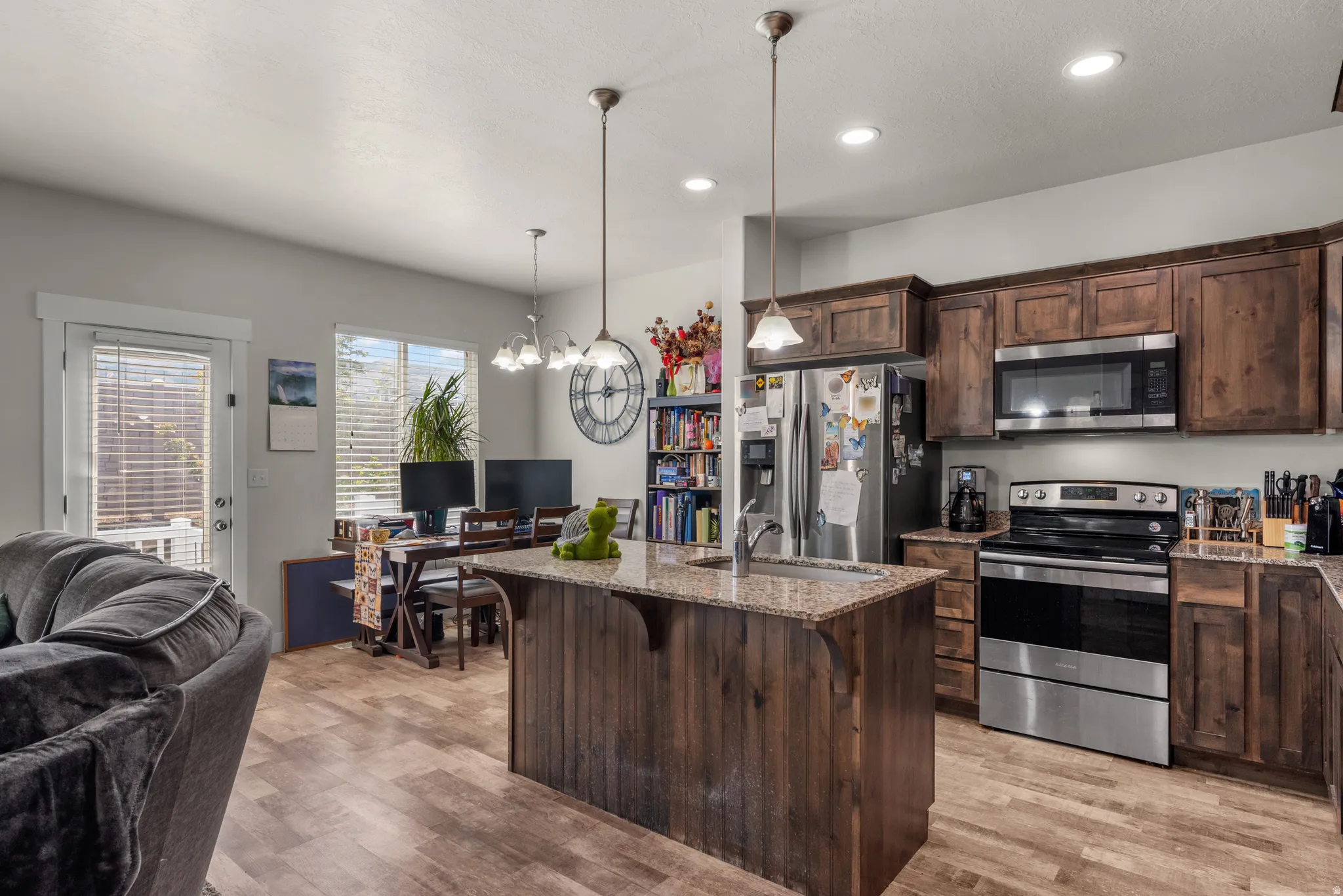 Open-concept kitchen featuring wood-finish flooring, dark wood cabinetry, a central island with a granite-style countertop, and stainless steel appliances