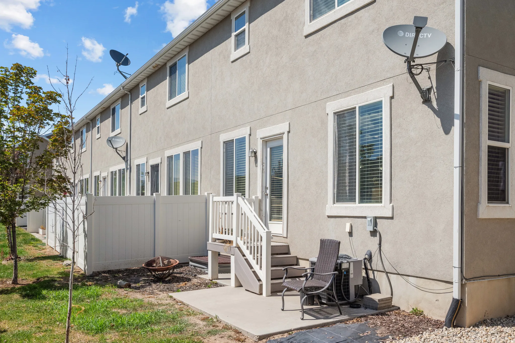 Rear exterior featuring a concrete patio, white vinyl fencing, and a private staircase leading to an upper-level entry