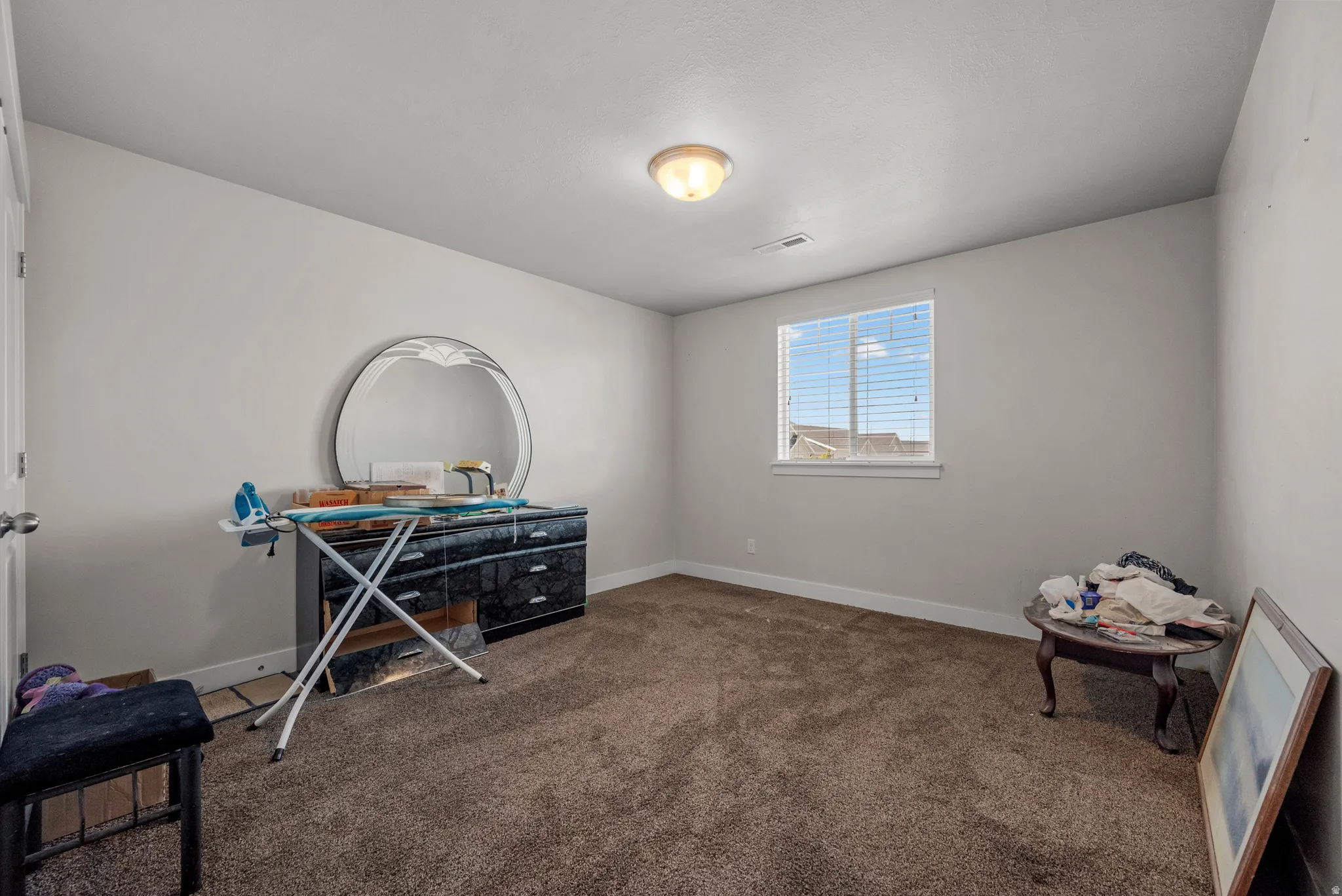 Neutral wall color with a contrasting white trim, featuring a single window with blinds and a ceiling-mounted light fixture