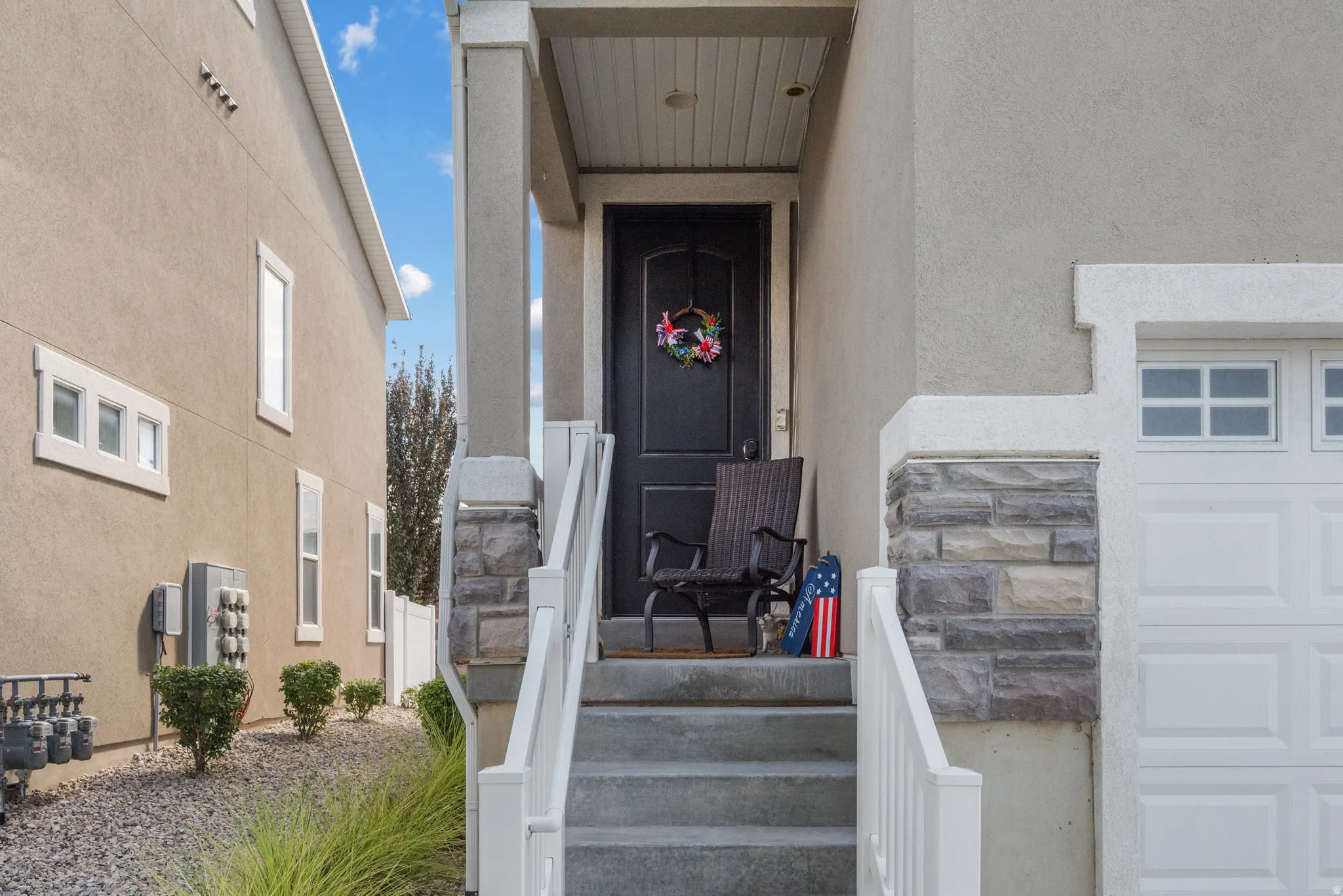 Front entry featuring a dark paneled door, concrete steps with white railings, and a stone facade accent