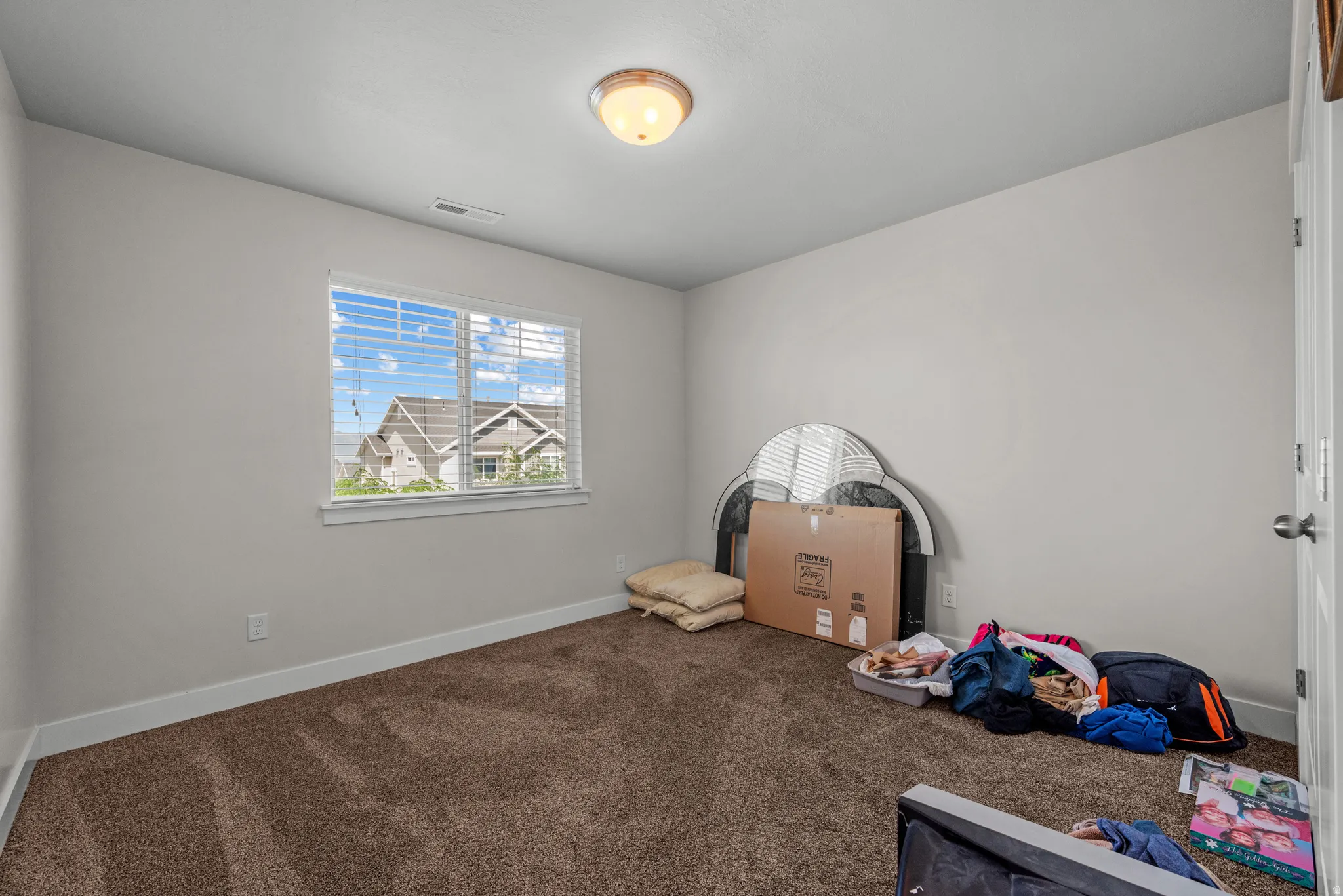 Bright bedroom featuring a large window with blinds, neutral wall paint, and brown carpeting