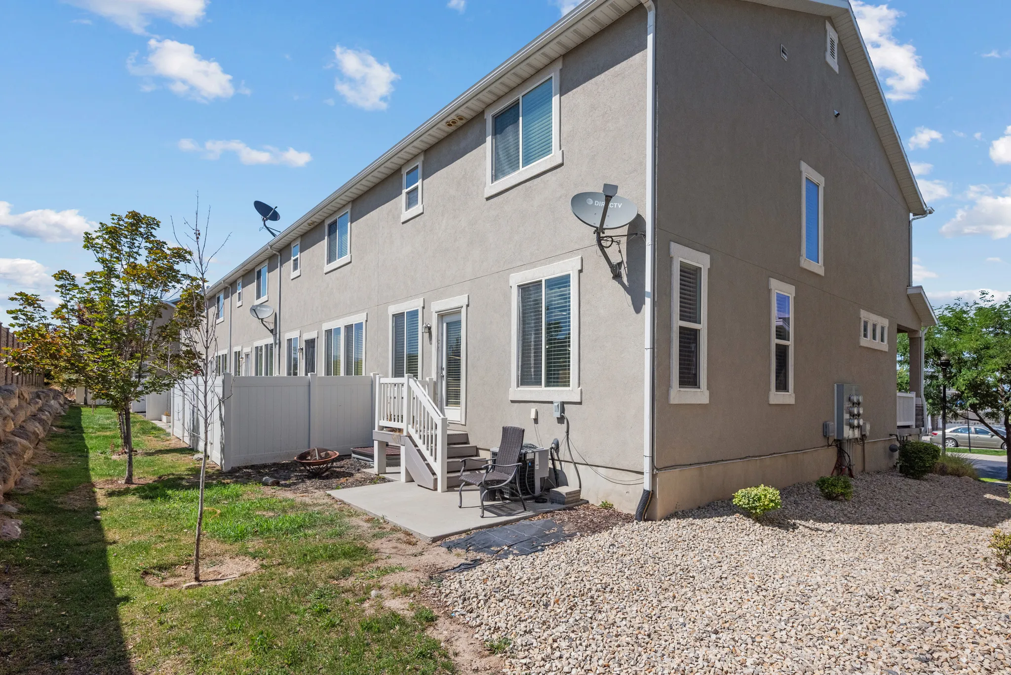 Rear exterior featuring a concrete patio with a privacy fence, multiple windows with white trim, and a gravel-landscaped area