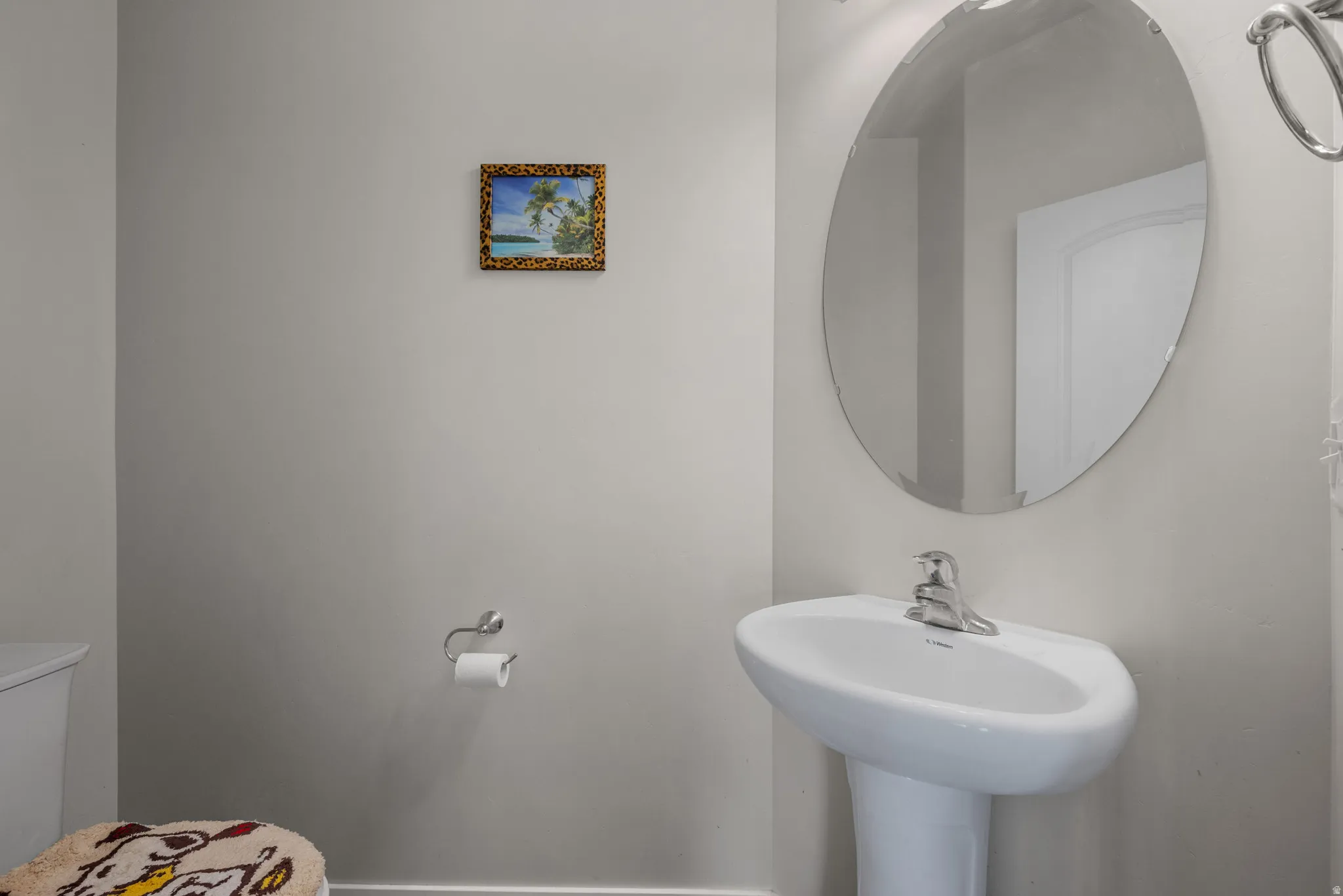 Pedestal sink with chrome faucet, complemented by an oval wall-mounted mirror