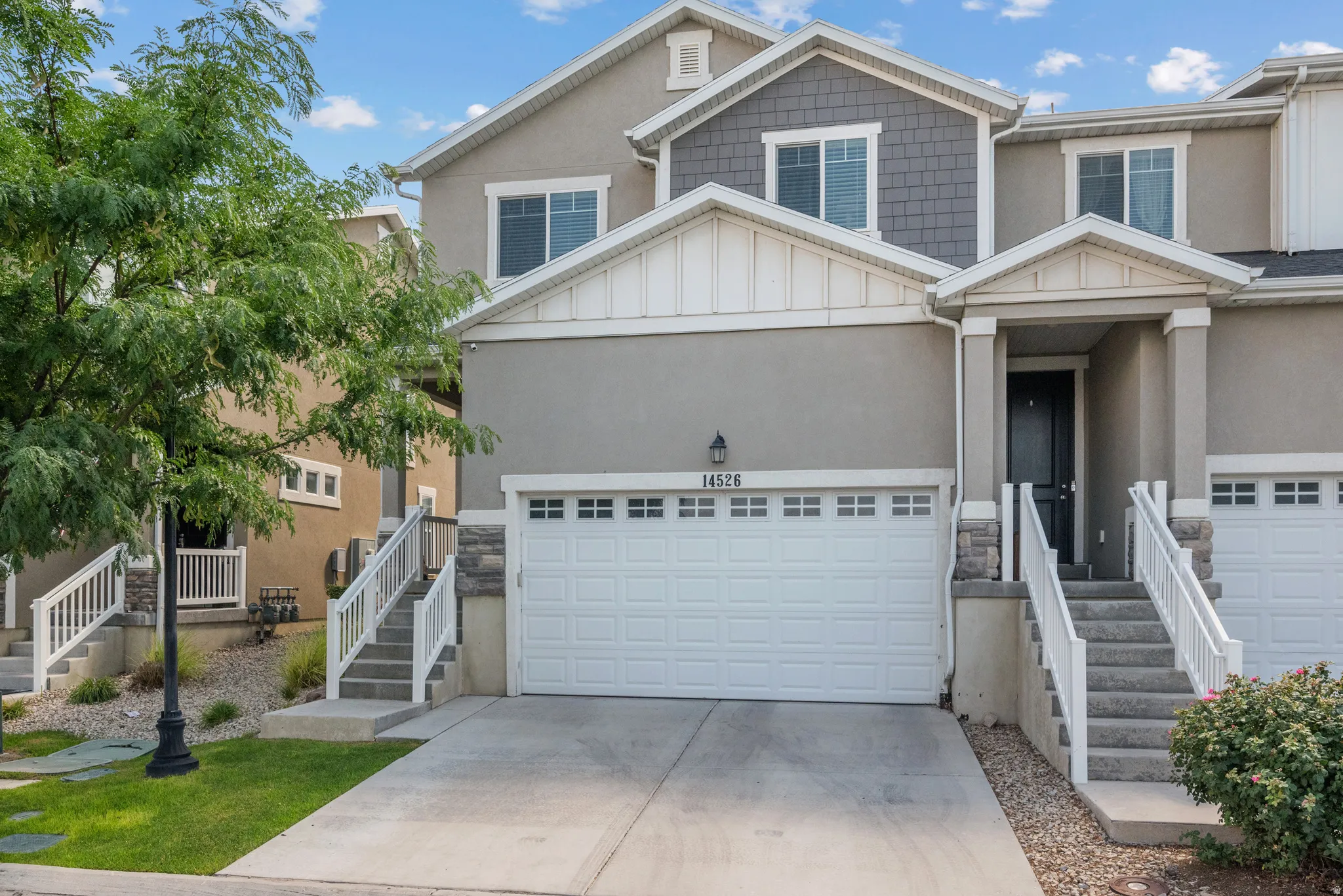 Two-story townhome with a light gray stucco exterior, a single garage, and a covered front entry
