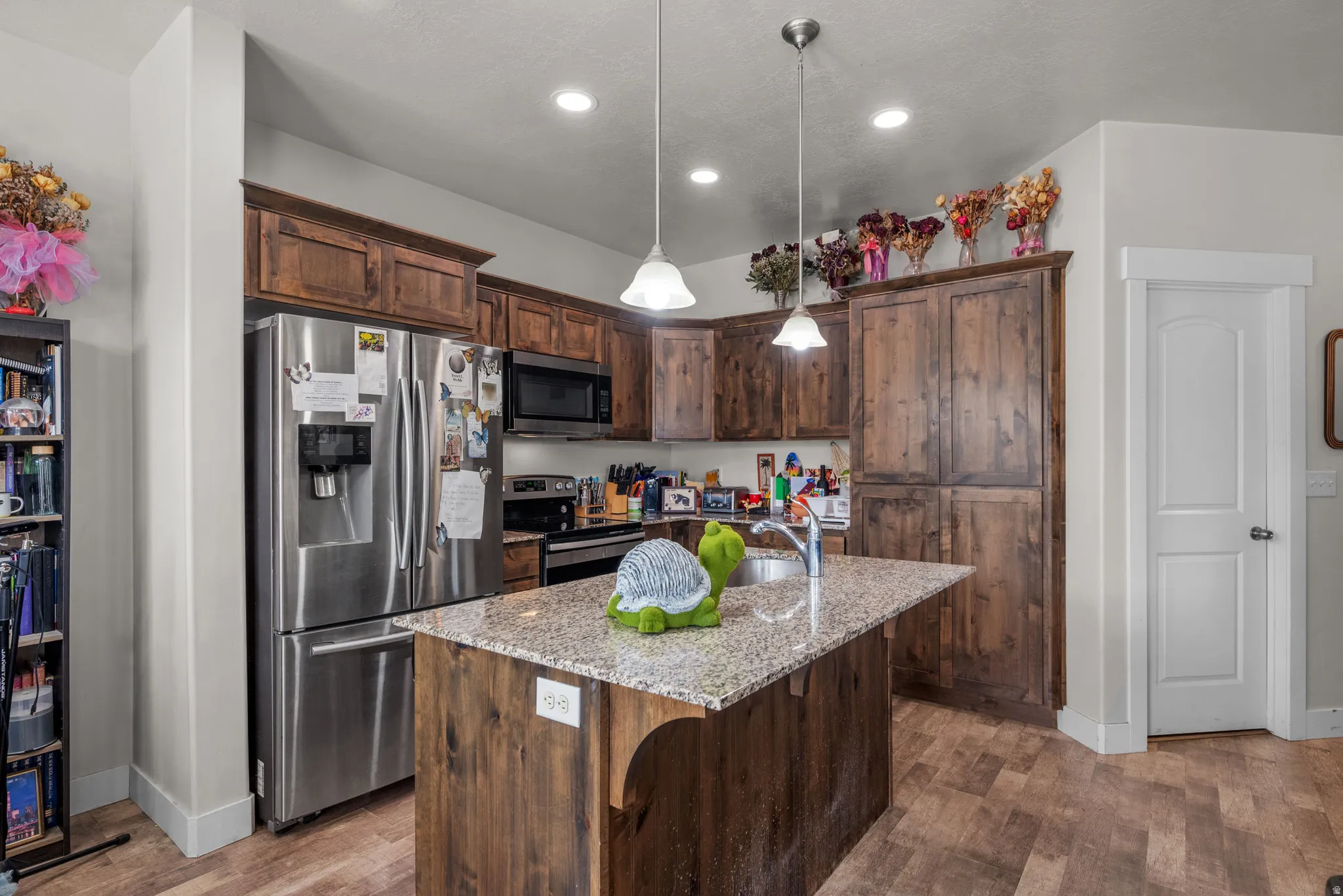 Kitchen featuring a granite-topped island with an undermount sink, recessed lighting, pendant lights, stainless steel appliances, and wood-finish cabinetry