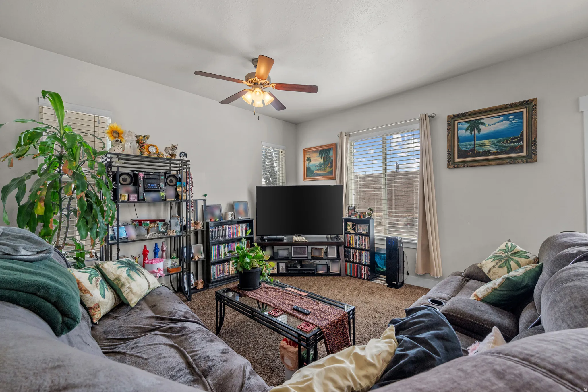 Living area featuring light-toned walls, brown carpet flooring, and a ceiling fan with integrated lighting