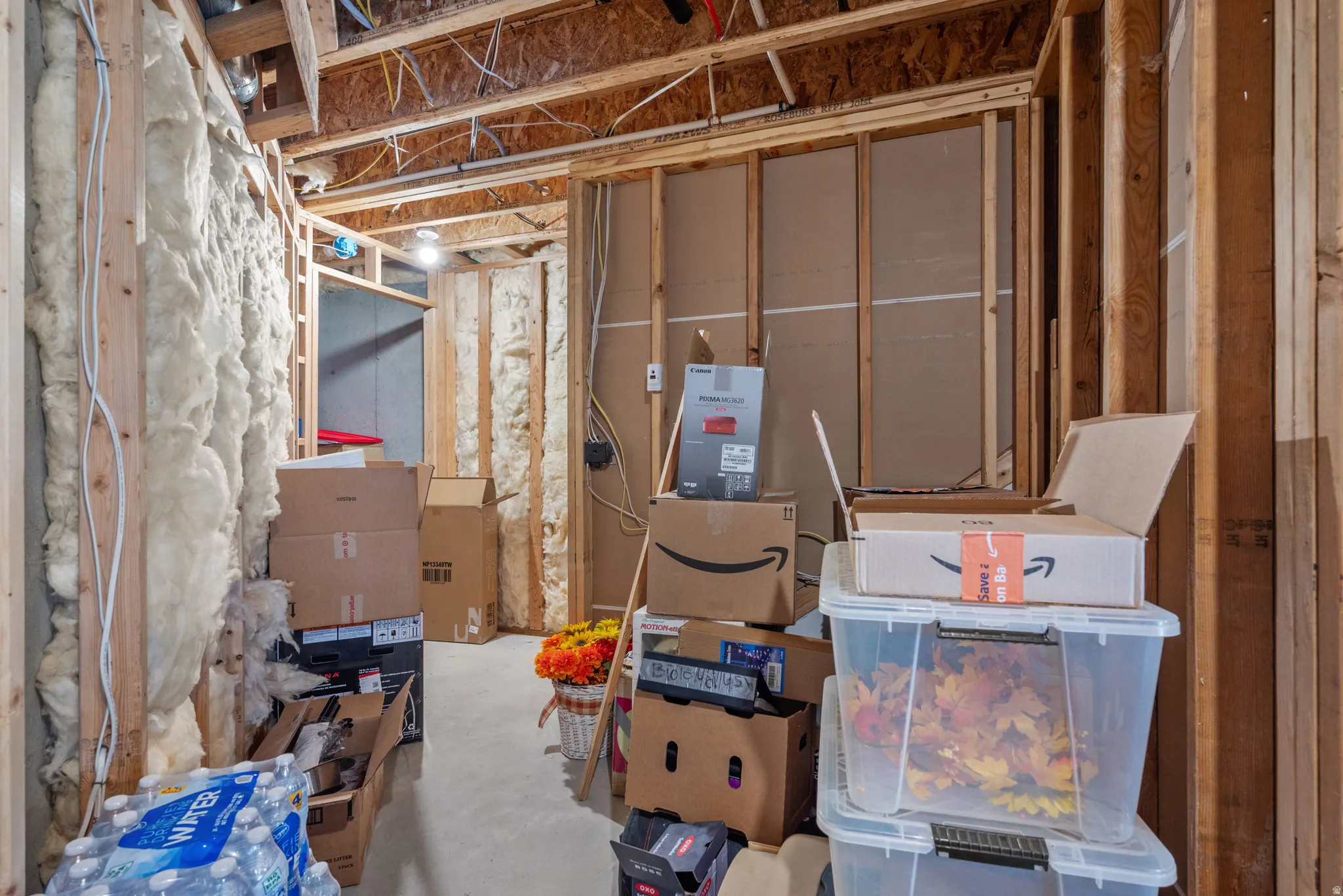 Unfinished basement area featuring exposed wood framing, ceiling joists, and visible insulation