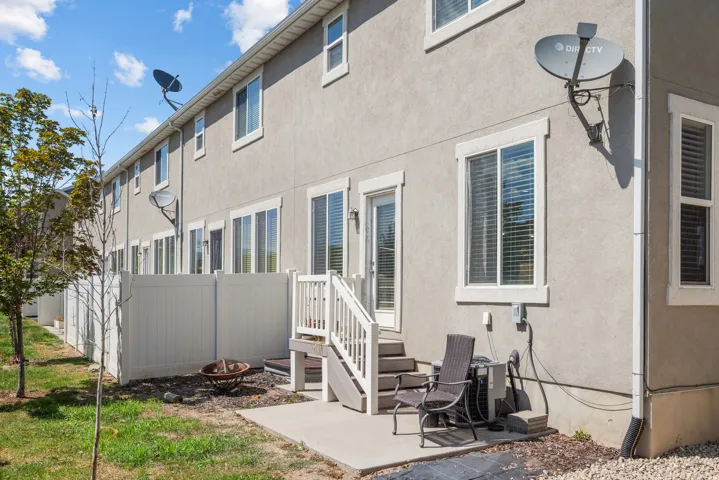 Rear exterior featuring a concrete patio, white vinyl fencing, and a private staircase leading to an upper-level entry