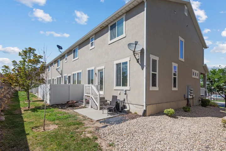 Rear exterior featuring a concrete patio with a privacy fence, multiple windows with white trim, and a gravel-landscaped area