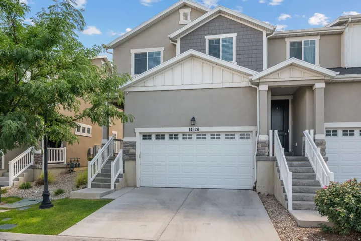 Two-story townhome with a light gray stucco exterior, a single garage, and a covered front entry