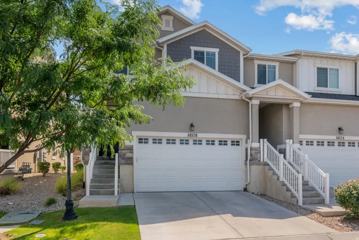 Contemporary townhome exterior featuring a stucco and siding facade, an attached garage, and a covered porch entry with white railings